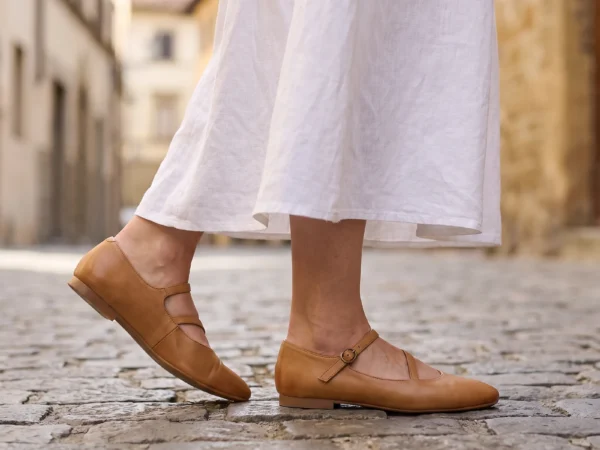 classic mary jane flats single strap soft sole comfort slip-on everyday shoes in apricot, worn on foot on a cobblestone old-town lane, soft daylight lifestyle photo