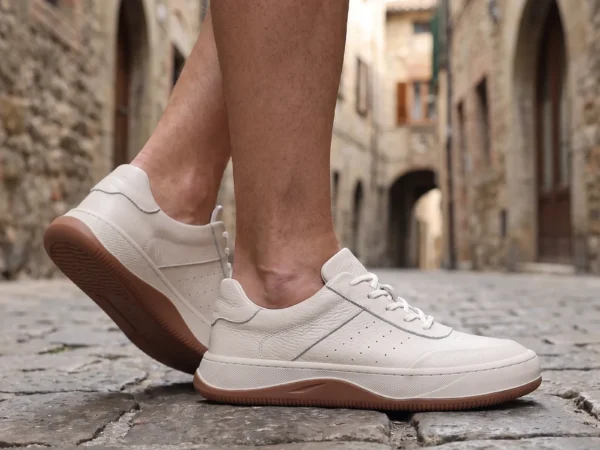 genuine leather casual sneakers breathable chunky sole in white, worn on foot on a cobblestone old-town lane, soft daylight lifestyle photo