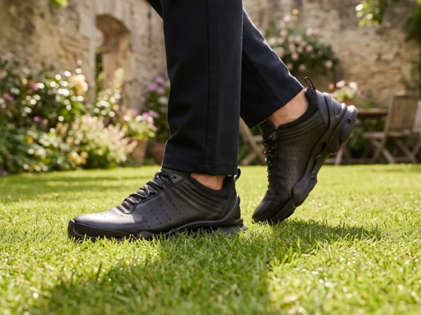 genuine leather business casual sneakers lightweight comfortable non-slip walking shoes in black, worn on foot on a garden lawn, soft daylight lifestyle photo