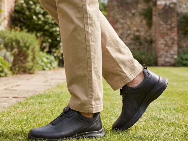 genuine leather rotating dial casual sneakers breathable lightweight in black, worn on foot on a garden lawn, soft daylight lifestyle photo