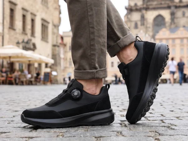 trendy rotating dial closure casual sneakers breathable chunky sole commuter shoes in black, worn on foot on a old-town square, soft daylight lifestyle photo