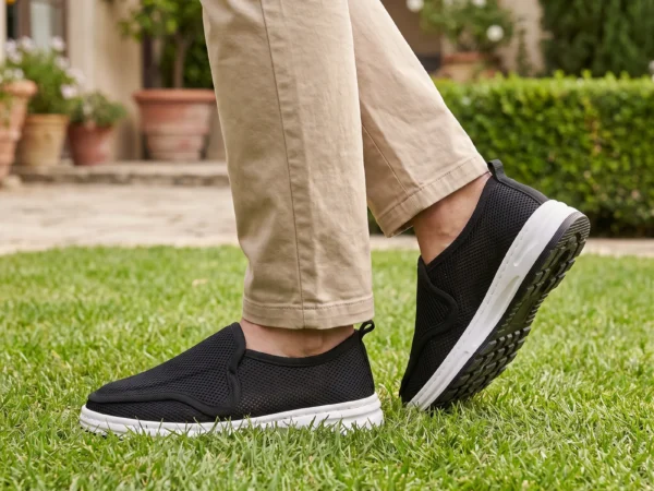 wide fit soft canvas slip-on shoes breathable mesh roomy toe everyday comfort in black, worn on foot on a garden lawn, soft daylight lifestyle photo