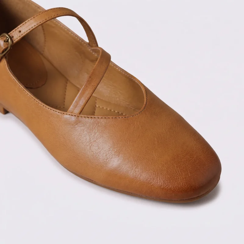Close-up of the rounded almond toe and crossed instep strap of apricot AZEKA Mary Jane flats