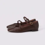 Pair of brown AZEKA French-retro single-strap Mary Jane flats, soft flat sole, front 45 degree view on light gray background