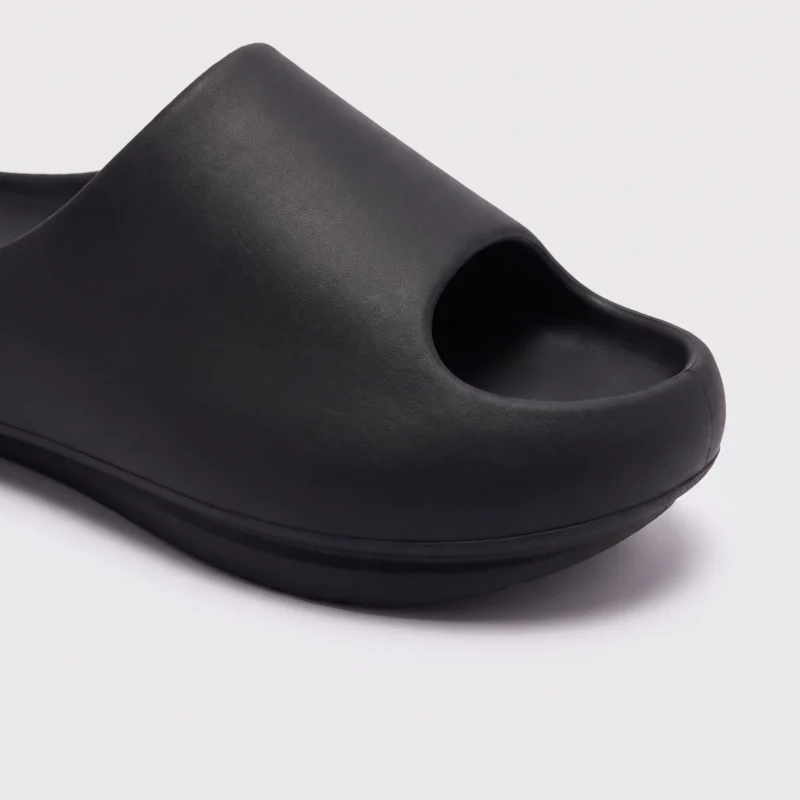 negative heel arch support slide sandals - thick platform one-piece eva slides for women in black, close-up view of the toe on a light gray background