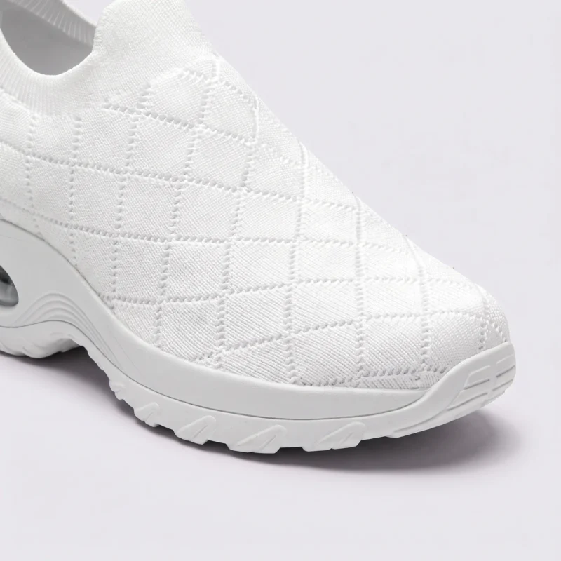 slip-on quilted sock sneakers - lace-free everyday shoes with a cushioned thick sole and heel window in white, close-up view of the toe on a light gray background