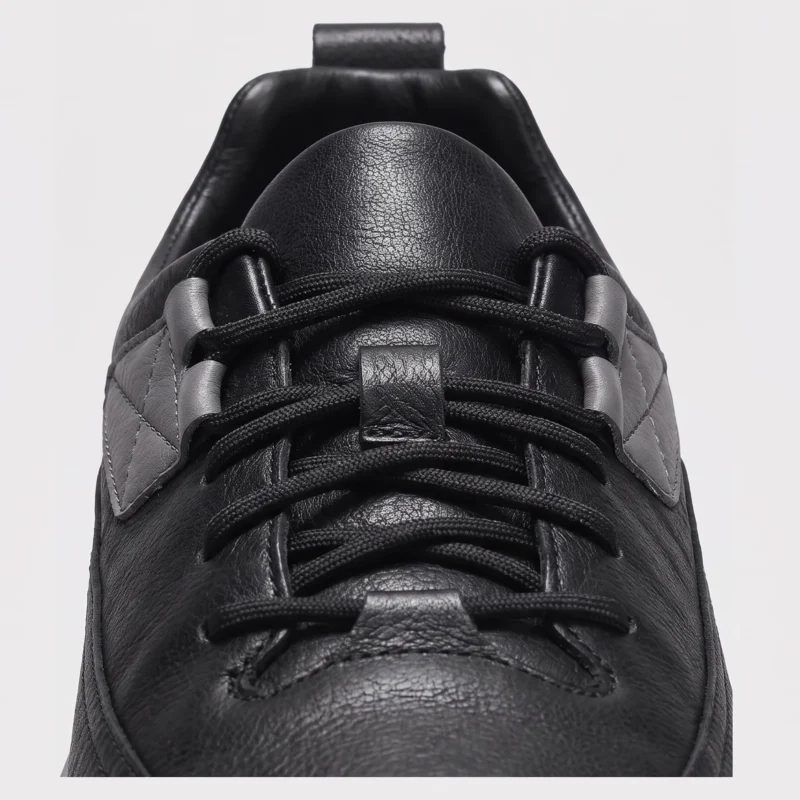 chunky sole leather casual sneakers in black, close-up view of the closure on a light gray background