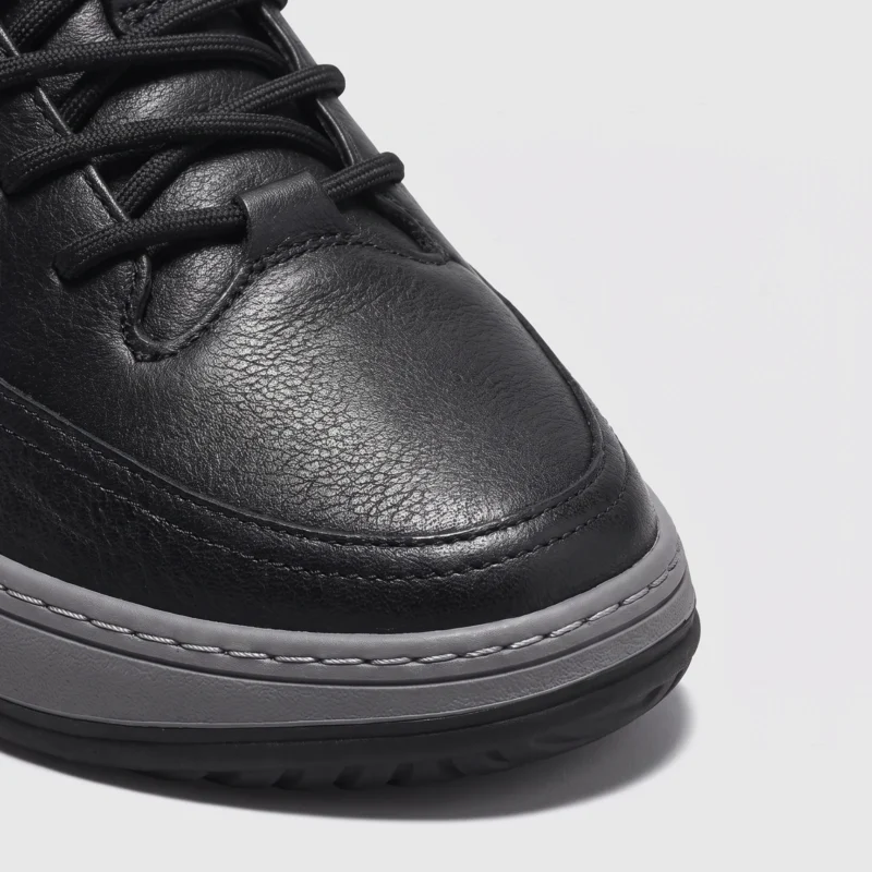chunky sole leather casual sneakers in black, close-up view of the toe on a light gray background