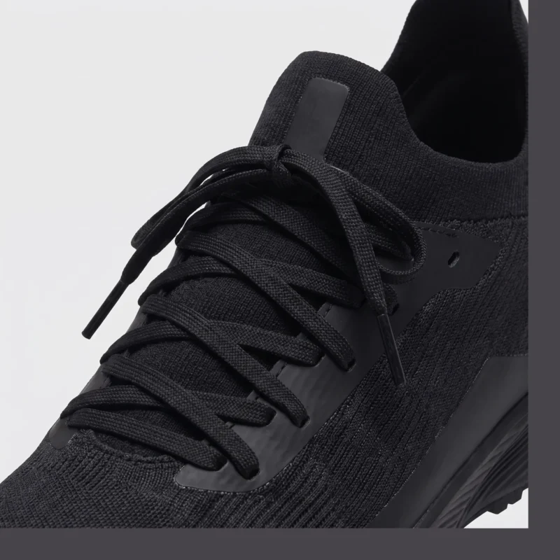 lightweight trail running sneakers in black, close-up view of the lace on a light gray background