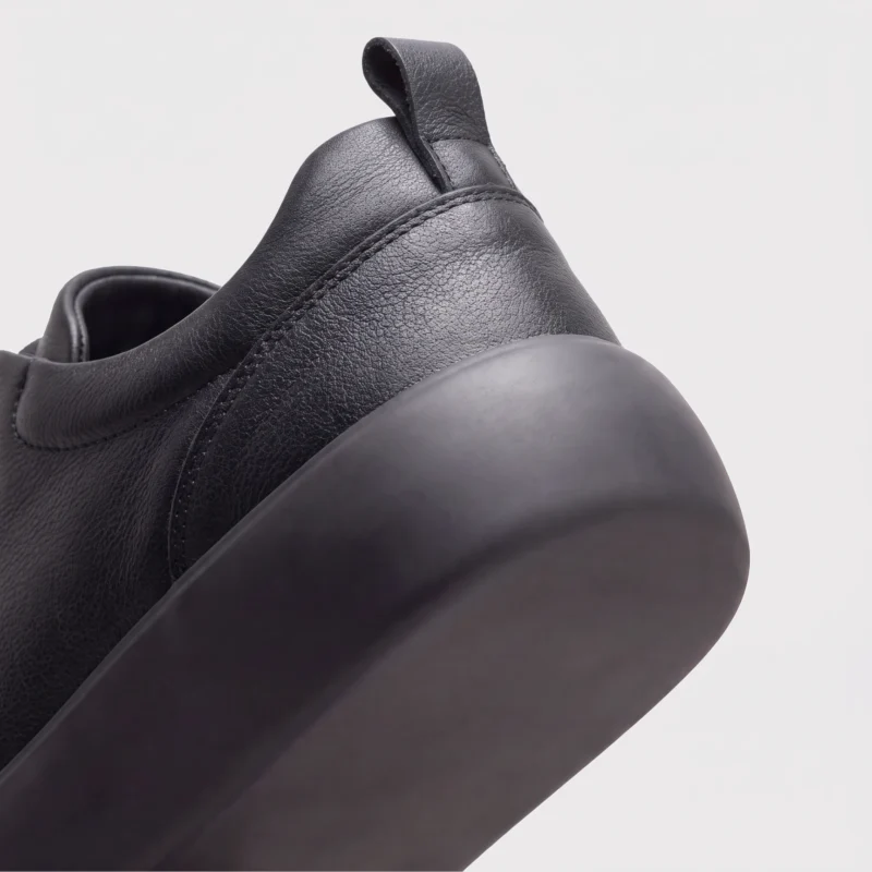 genuine leather business casual running sneakers in black, close-up view of the heel on a light gray background